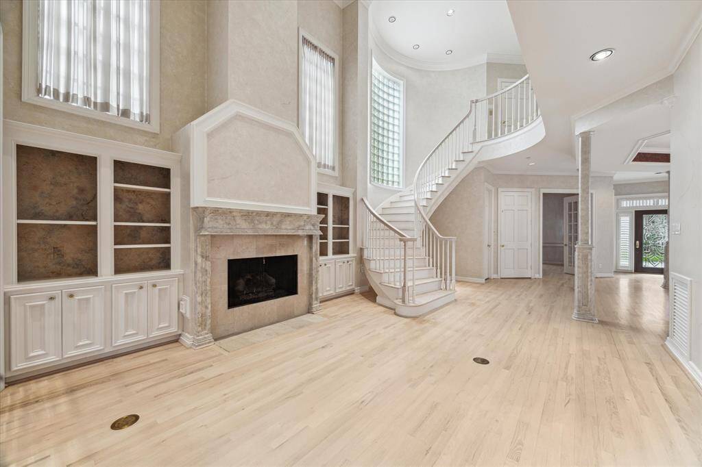 Living room with custom built-ins, gas- log fire place with marble surround.  Natural light from large upper windows illuminates the space.