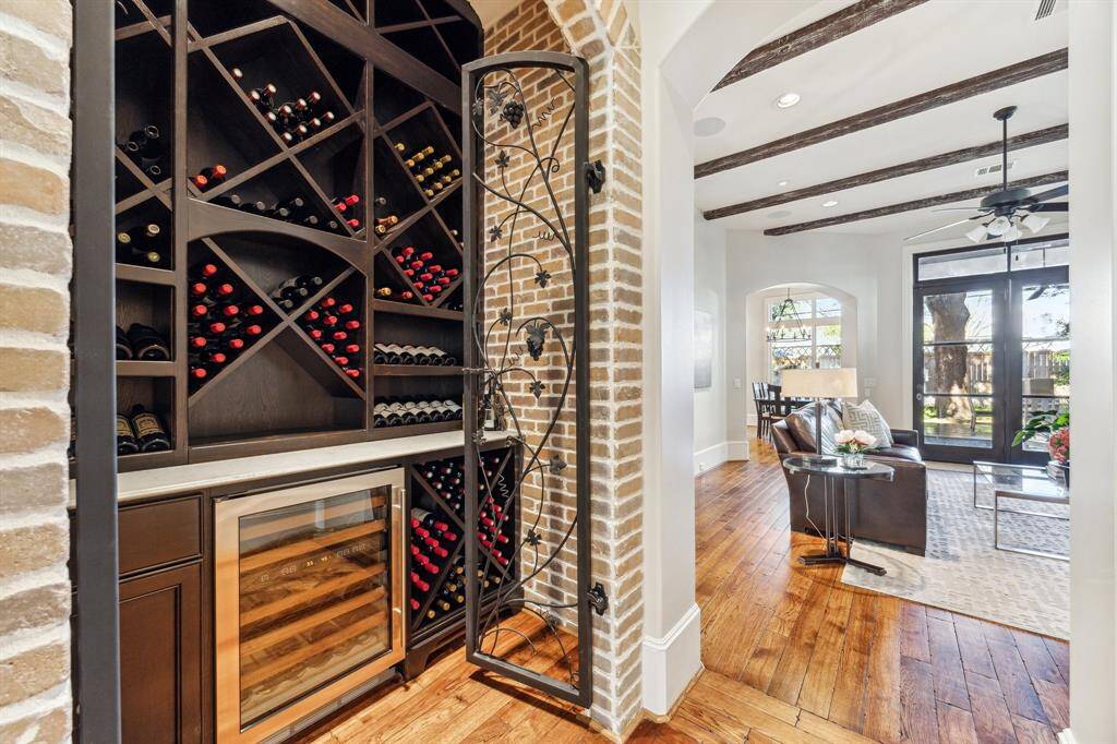 View of brick-clad wine room with built-in wine fridge and through to family room. This threshold between family room and living room features a framed herringbone inlaid hardwood floor.