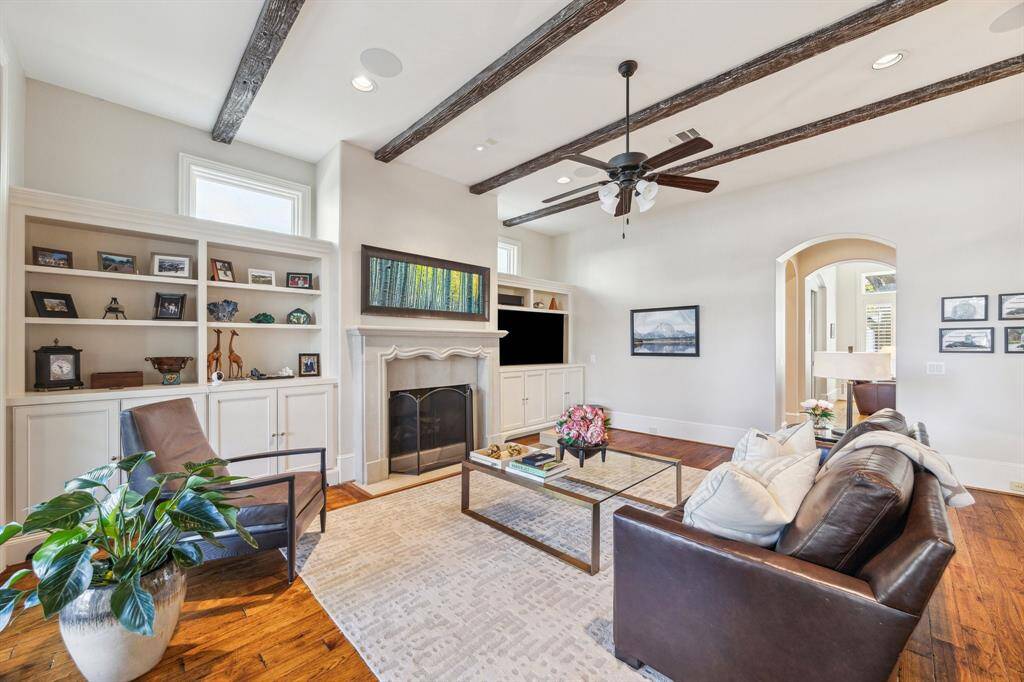 A view of the family room featuring wood-burning or gaslog fireplace, abundant storage/display, art-lighting, and surround-sound audio/video built-in entertainment components. The ceiling is beamed, and the floors are rich hardwood. The house has LED flood-lighting throughout.