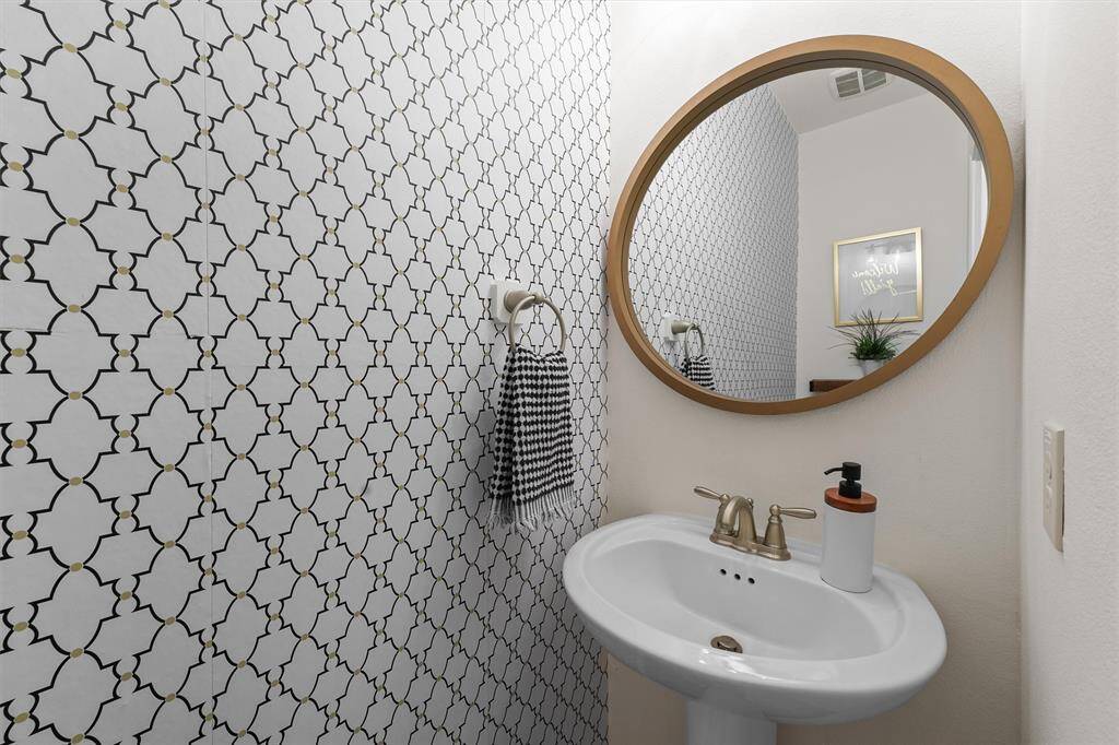 The powder room is a stylish retreat, featuring eye-catching wallpaper and a custom mirror.  It's a welcoming atmosphere for guests.