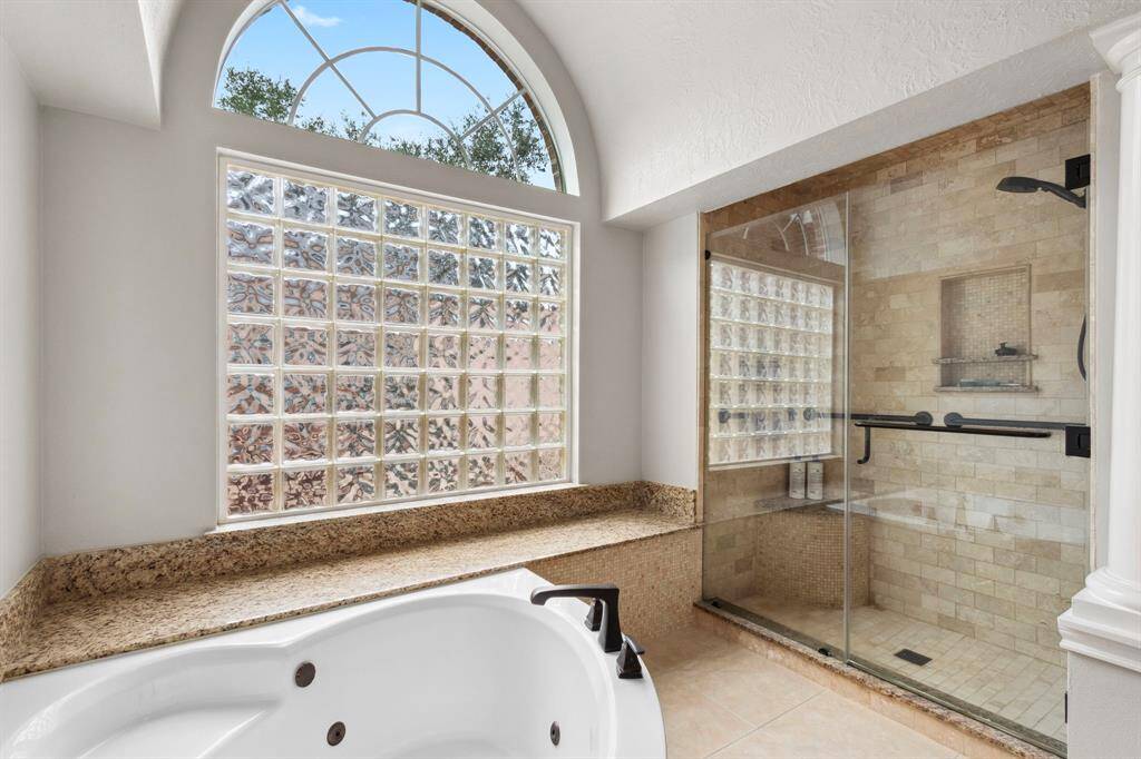 Travertine stone tile adorns the walk-in shower with full glass doors, seating & shampoo shelf.