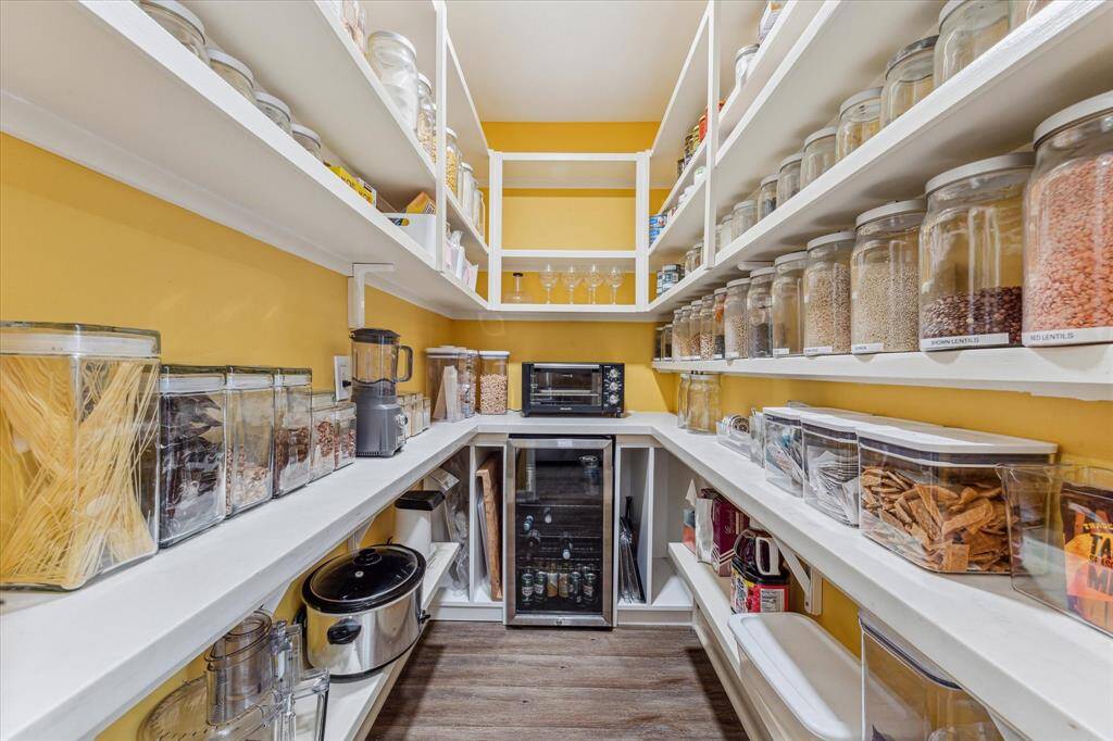 The spacious walk-in pantry offers floor-to-ceiling shelving for effortless organization and includes a built-in beverage chiller, making it as functional as it is convenient.