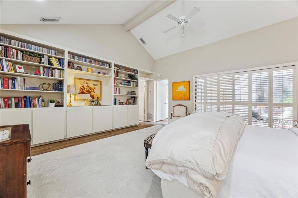 The primary bedroom suite impresses with a soaring cathedral ceiling, expansive shuttered windows that bathe the space in natural light, and stylish wood-look tile flooring, creating a spacious and relaxing retreat.