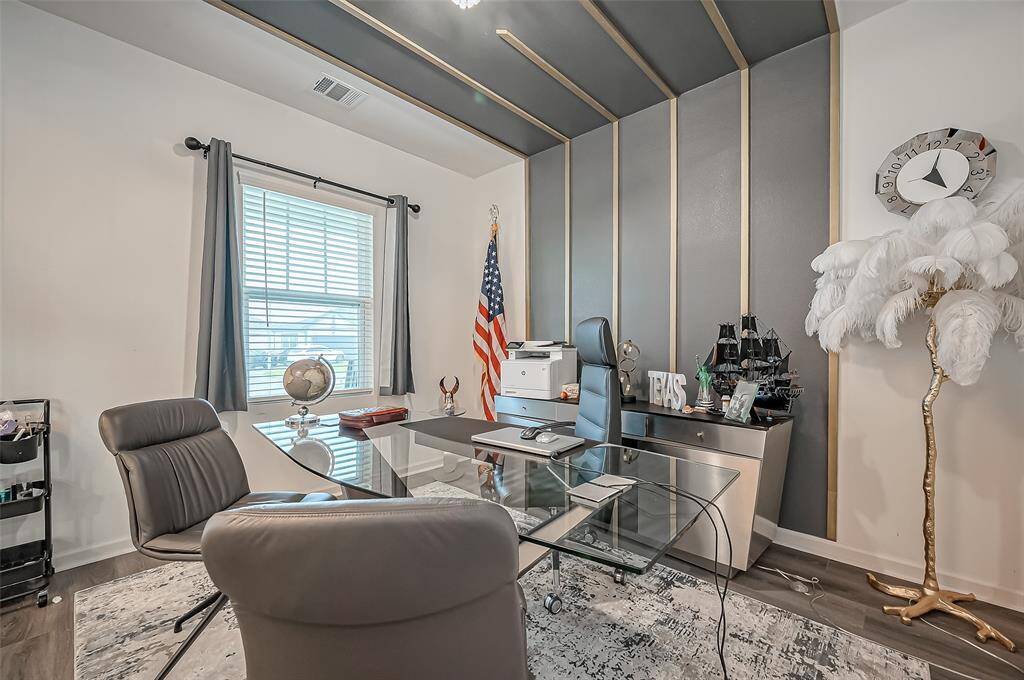 A sophisticated and professional space, this office features a bold accent wall with the design extending to the ceiling. A large window brightens the room, while nearly full-wall glass doors add an element of openness and refinement.