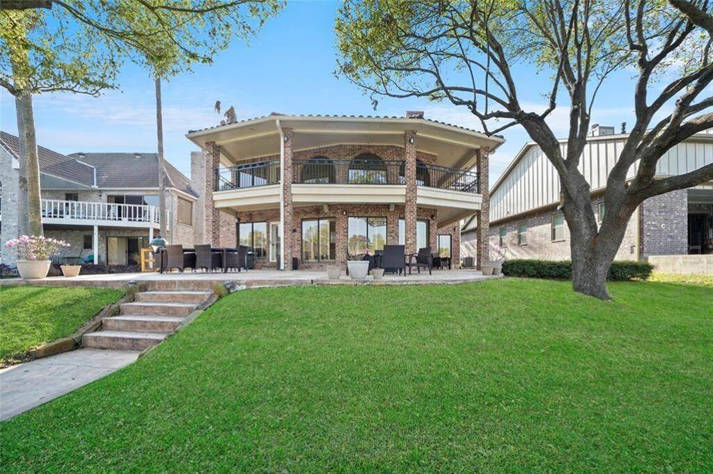 This photo showcases a two-story, brick home with large, covered balconies on both levels overlooking a spacious, well-maintained lawn. The outdoor area features ample seating and mature trees, offering a serene and inviting atmosphere.