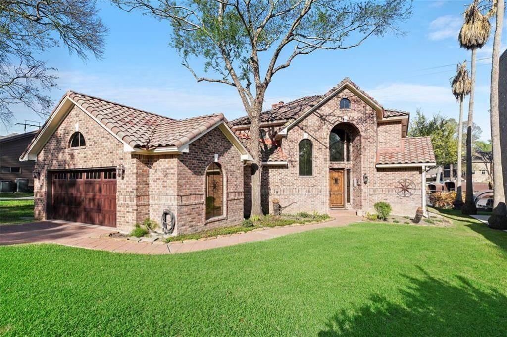 Charming brick home with a classic tile roof, beautifully framed by mature trees and lush green lawn.