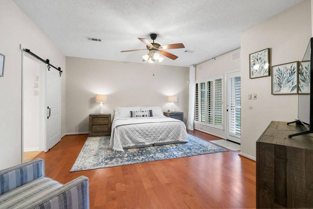Serene primary bedroom featuring warm hardwood floors, ample natural light through elegant French doors, and a charming barn door entry.