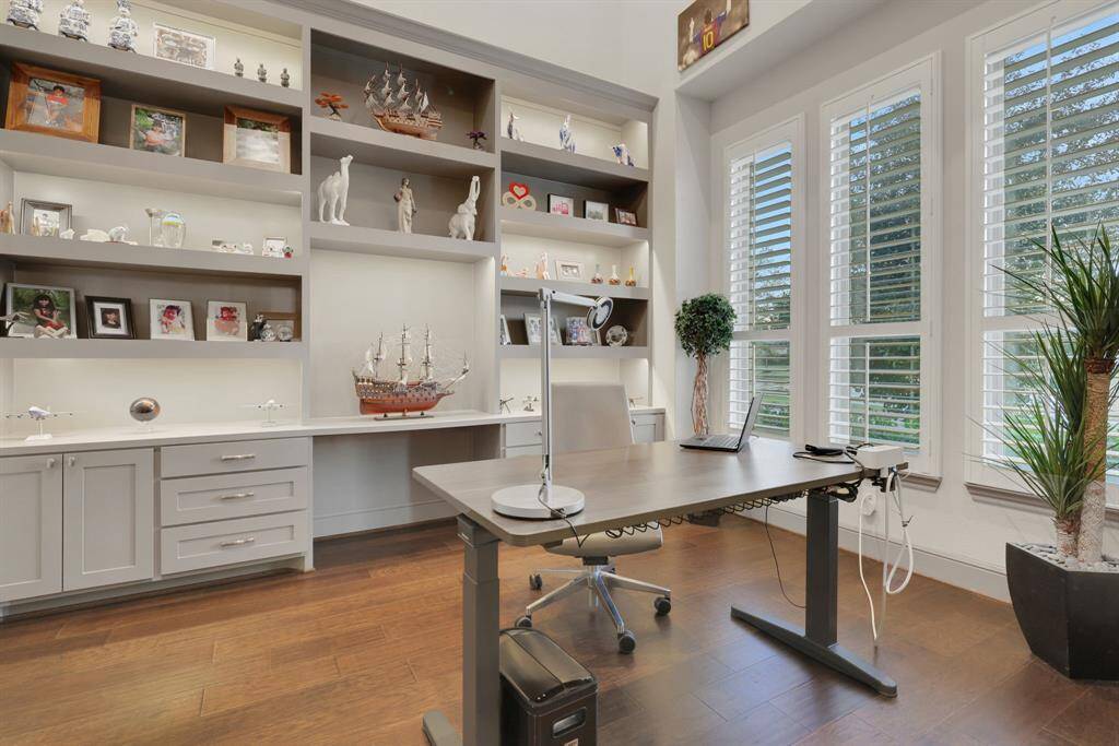 The bright, modern home office with built-in shelving, large windows with plantation shutters.