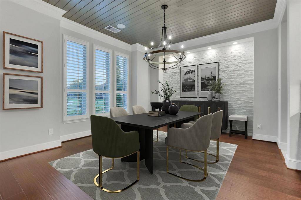 This dining room features is brightened by large windows with shutters, a light accent mosaic stone wall, and a decorative ceiling.