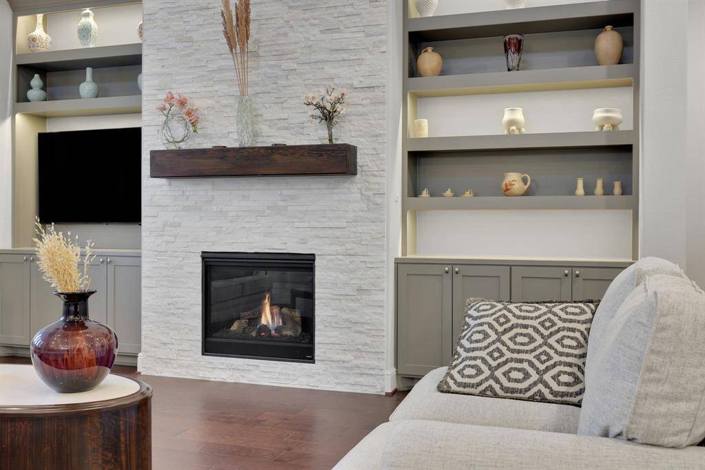 This inviting living room features a modern gas fireplace with mosaic stone surround and a dark wood mantel and built-in shelving.