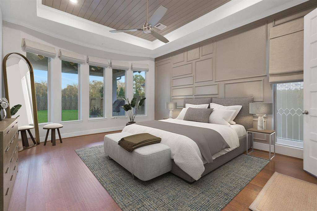 The modern primary bedroom with a spacious layout. It features a stylish textured accent wall, and abundant natural light from a row of tall windows. The room is enhanced with a ceiling fan, wood flooring, and customer wood work on the ceiling.