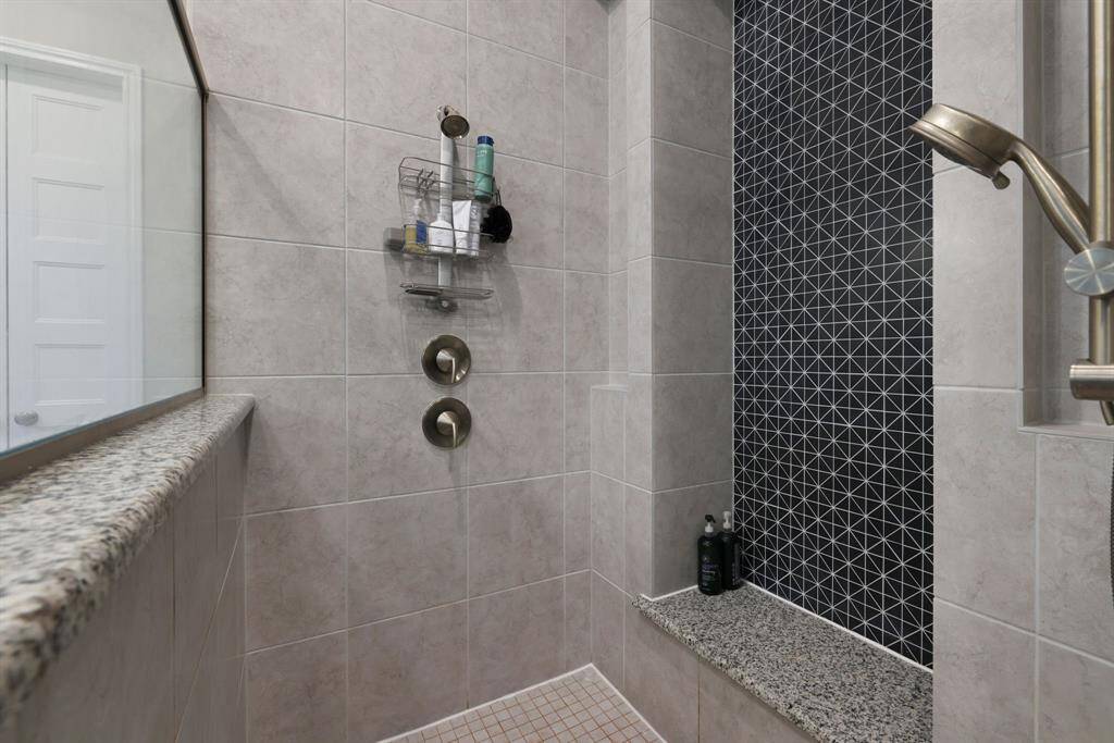 Modern shower with elegant tile work, featuring a mix of neutral and patterned designs. The shower includes a convenient built-in shelf, a sleek showerhead, and a niche for toiletries.