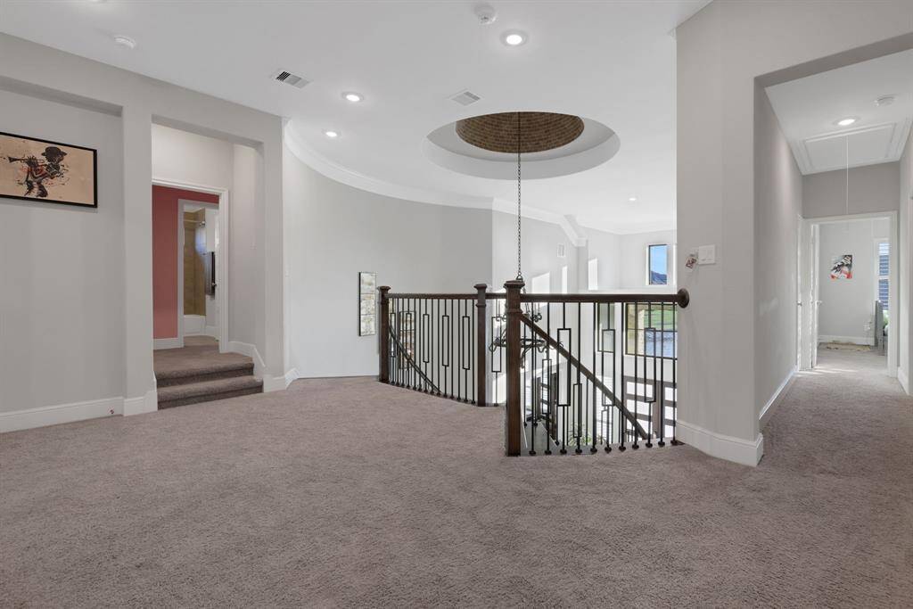 The spacious, upstairs landing area with a modern upgraded railing overlooking the staircase and living area below. The space features recessed lighting, multiple doorways leading to other rooms, and a large window providing natural light.