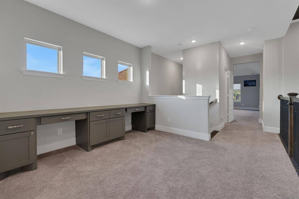 Built-in desks and cabinets, ideal for a home office or study area. Natural light streams through three small windows, enhancing the open and airy feel.