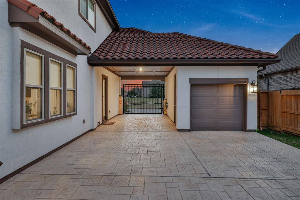 The modern home exterior with a covered driveway and a single-car garage. The house has a tiled roof and large windows, and there's a gated entrance leading to a backyard.