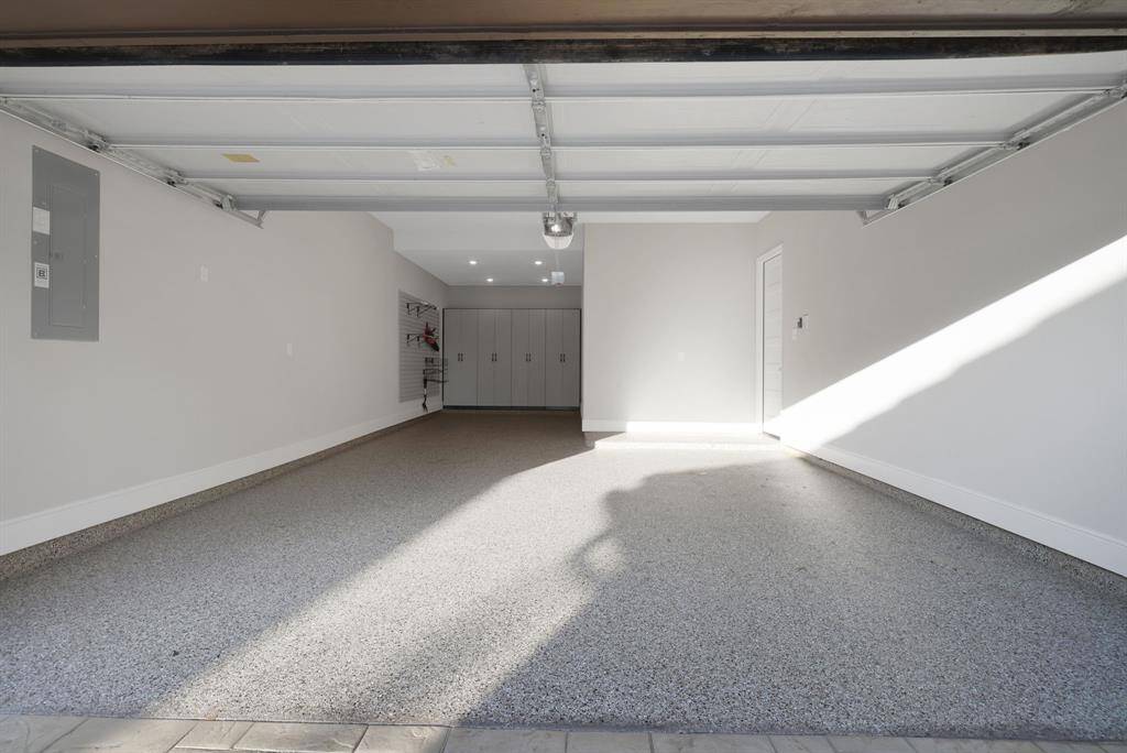 The spacious three-car tandem garage with a clean, finished interior. It features a polished concrete floor, built-in storage cabinets, and wall-mounted organization systems, offering ample storage and workspace. The space is well-lit with LED overhead lighting and includes a side access door to the home.