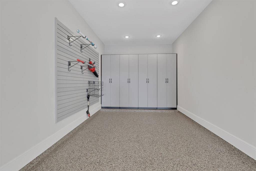 The three-car tandem garage has spacious storage area with sleek cabinets and a slat wall for hanging tools, set against a clean, modern design with a epoxy floor and recessed lighting. Ideal for an organized workspace or garage.