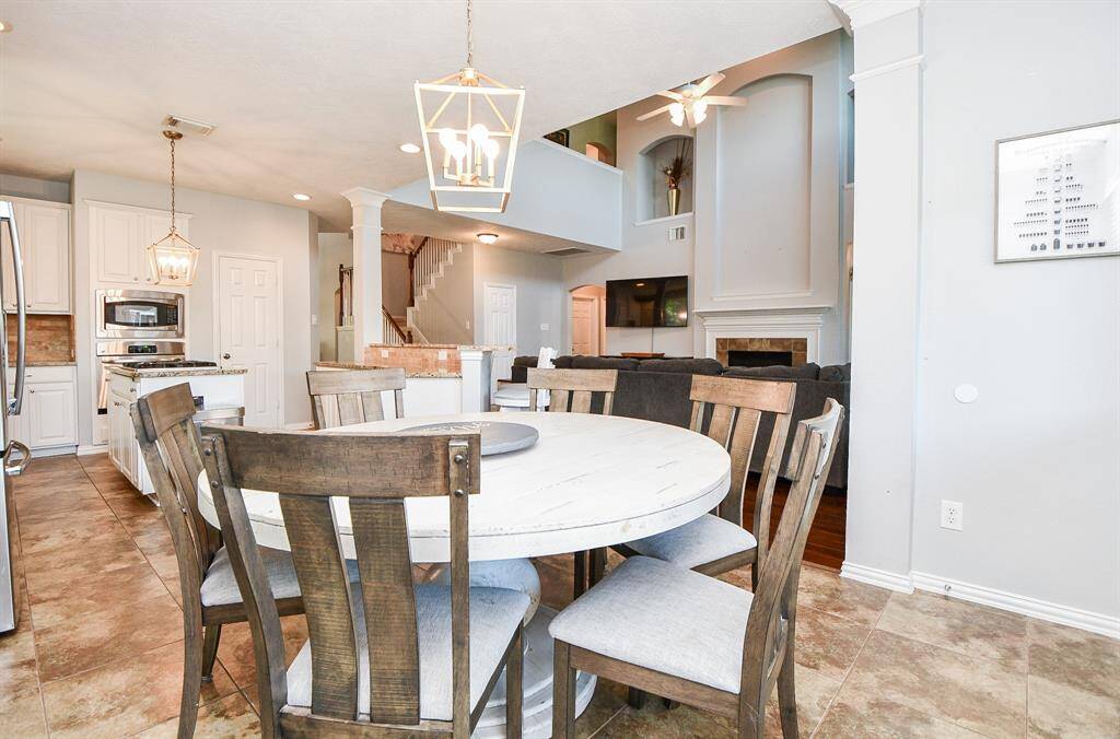 This photo showcases an open-concept living area with a cozy dining space and modern kitchen. The kitchen features sleek stainless steel appliances and an island. The living area has a vaulted ceiling, a large TV, and a fireplace, creating a warm and inviting atmosphere.