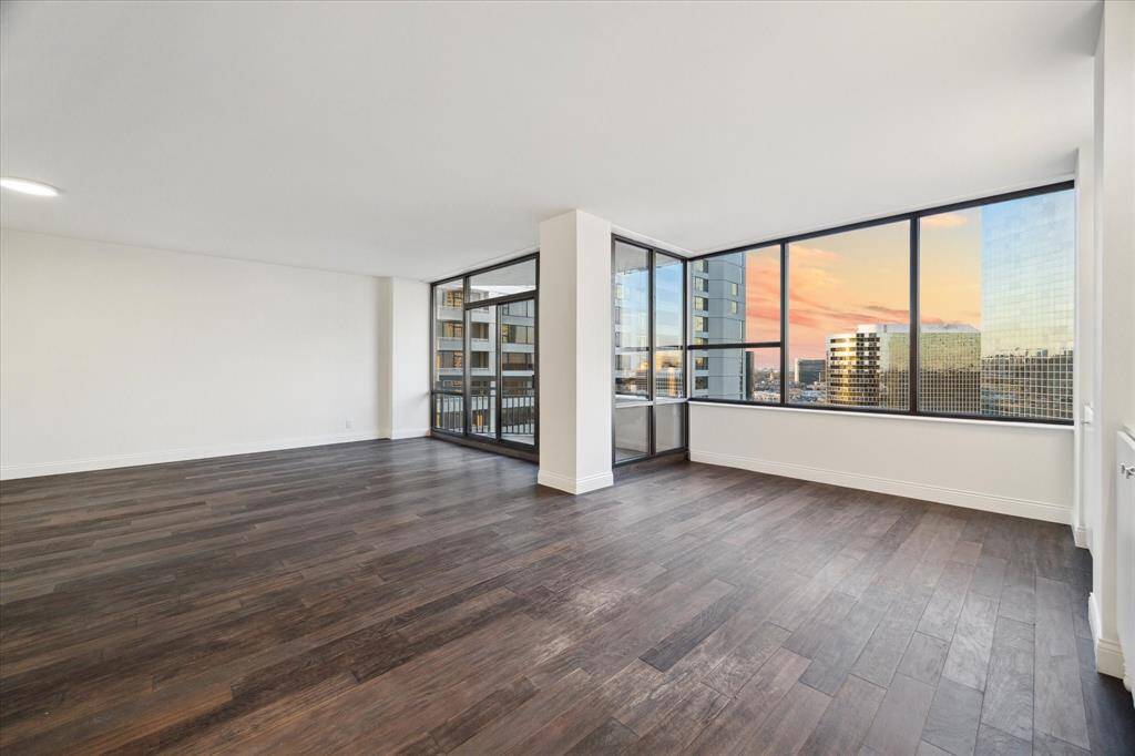 This spacious, modern living area features large windows offering stunning cityscape views with a beautiful sunset backdrop. Perfect for enjoying natural light and an open atmosphere.