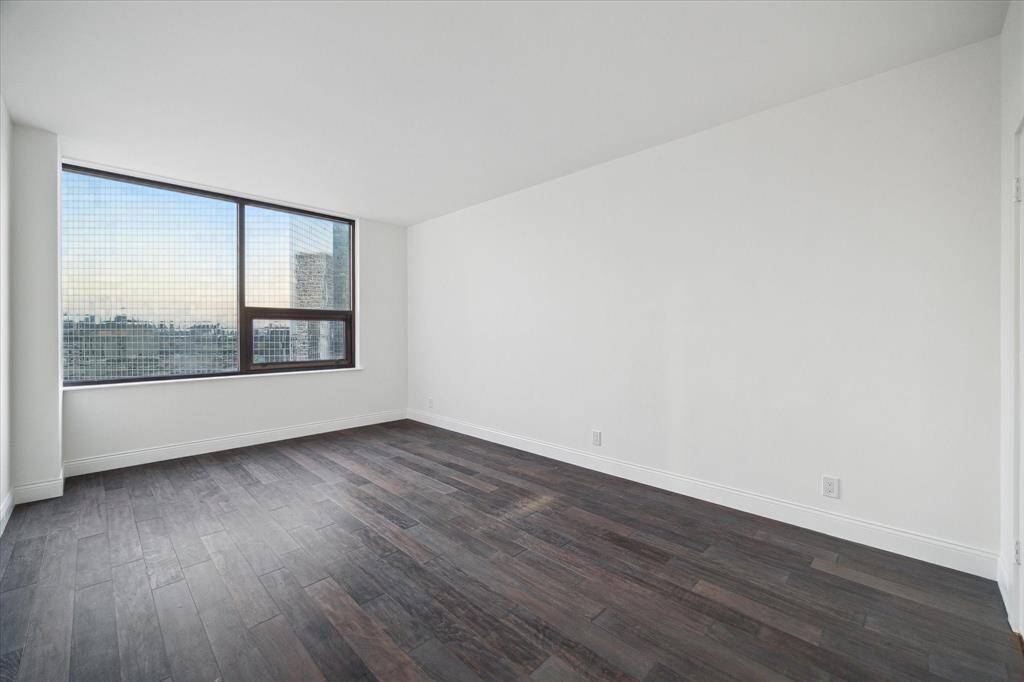 Bright, spacious room with large windows offering city views, hardwood floors, and white walls creating a modern, clean look where you can display large-scale artwork.