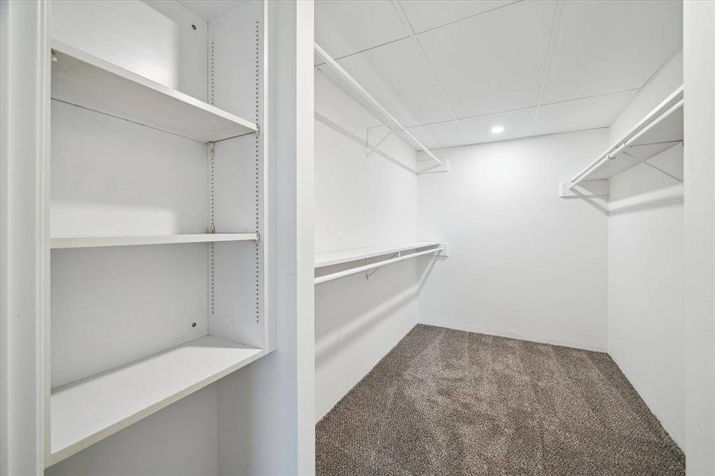 Spacious walk-in closet with white walls, built-in shelving, and ample hanging space. The newly carpeted floor adds warmth, while recessed lighting ensures good visibility. Ideal for organized storage.