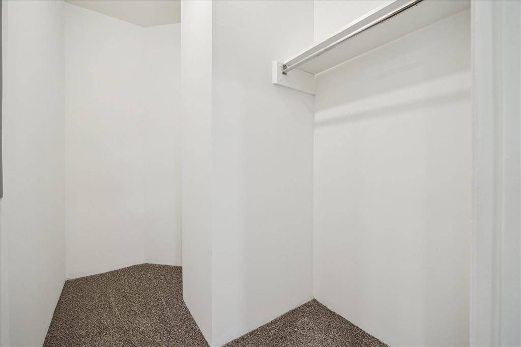 A spacious walk-in closet with white walls and a newly carpeted floor. It features a single hanging rod for clothing storage.
