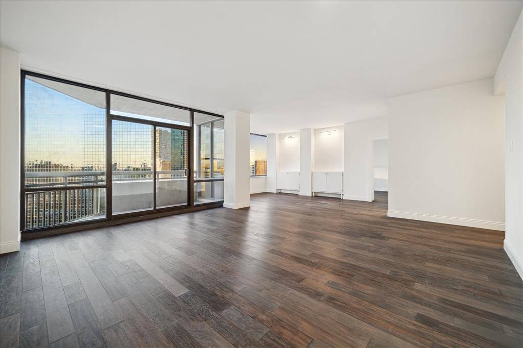 This photo showcases a spacious, light-filled living area with elegant dark wood flooring and new cabinetry.