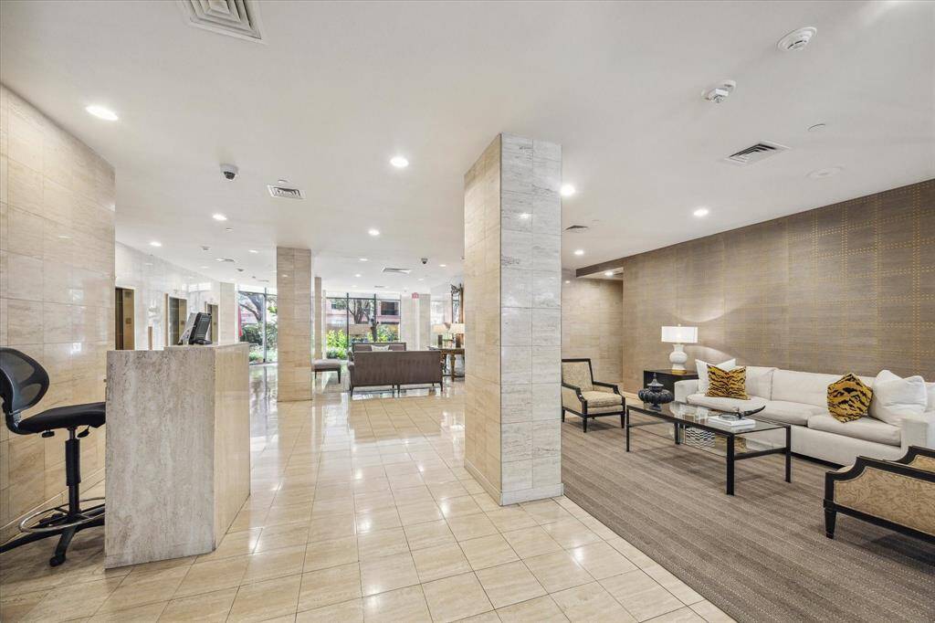 This is the welcoming lobby where you will be greeted by the doorman/concierge. It features a comfortable seating area with a sofa and chairs, a reception desk, and large windows allowing natural light. Ideal for a first impression in a residential building.