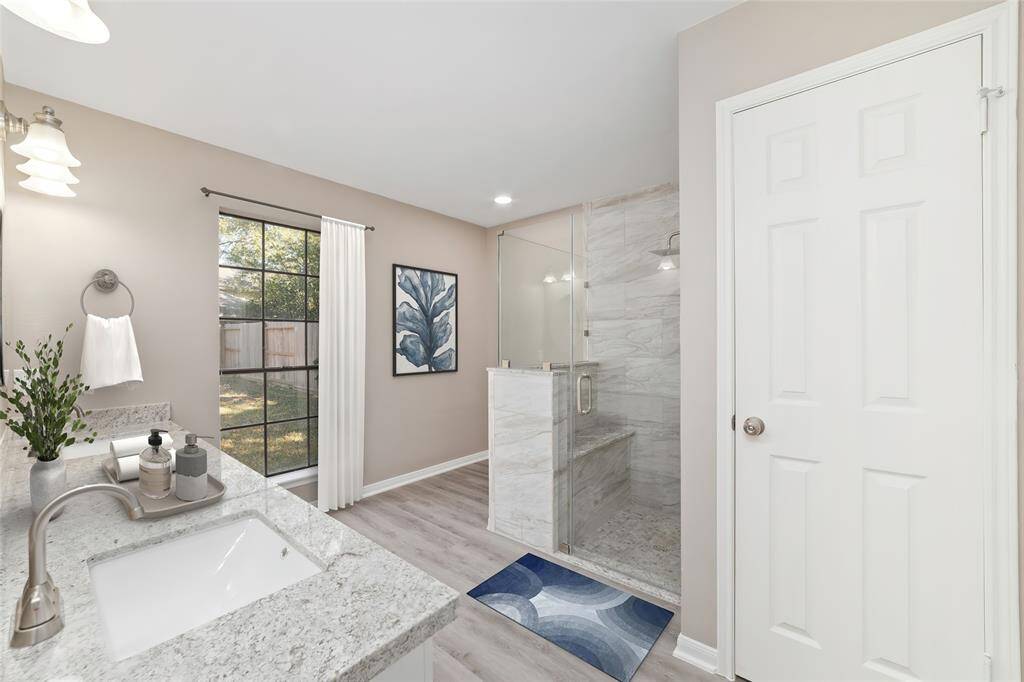 Tranquil primary ensuite bathroom with its soothing neutral color palette and clean design featuring a granite countertop with twin undermount sinks, and marble-style tile in the custom frameless shower. Virtually staged.