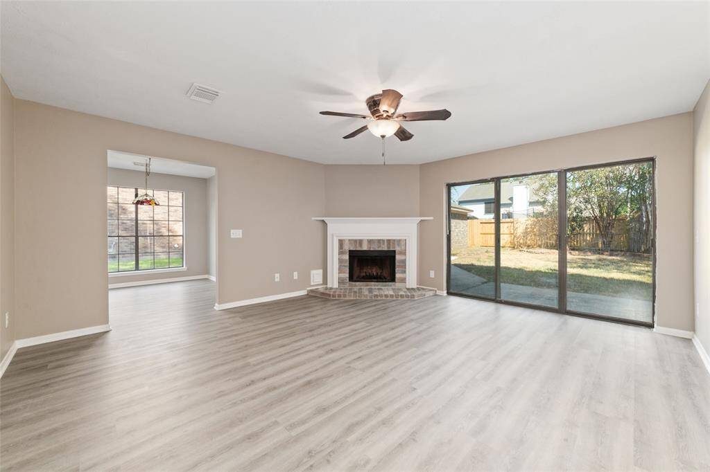 Spacious living room with modern luxury vinyl plank flooring, abundant natural light, a gas fireplace, and direct access to the backyard through the sliding glass door.