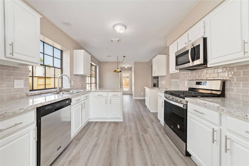 An alternate view of the kitchen, showing unimpeded access between the gas oven/range and the sink, a dedicated informal dining area, and further along in the hallway is a private powder room for guests and a laundry area.