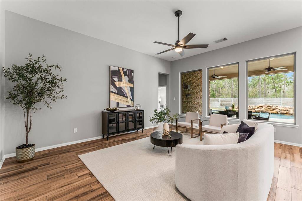 This bright, open-concept living area boasts its modern feel and versatile layout. Large windows invite natural light and offer views of the patio and surrounding greenery and pool, enhancing the airy ambiance.