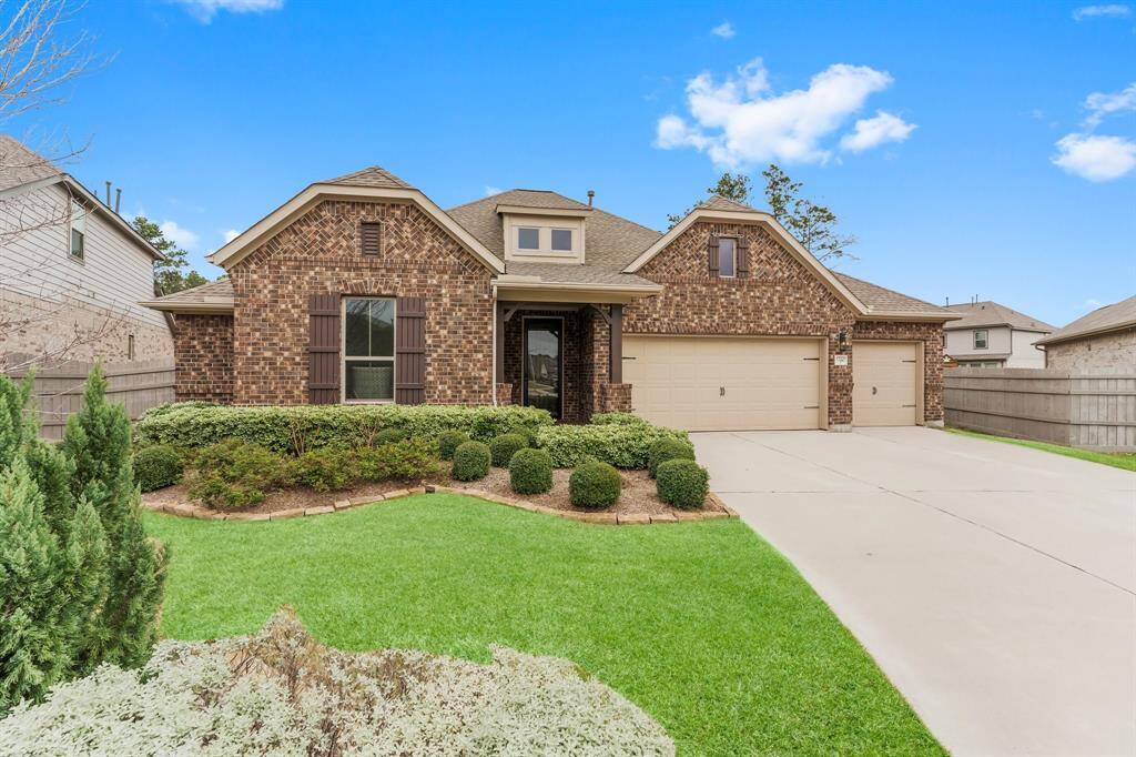 This charming brick home features a well-maintained front yard with lush landscaping. It has a spacious driveway leading to a three-car garage, and the architecture includes a mix of traditional and modern elements with a welcoming entrance.