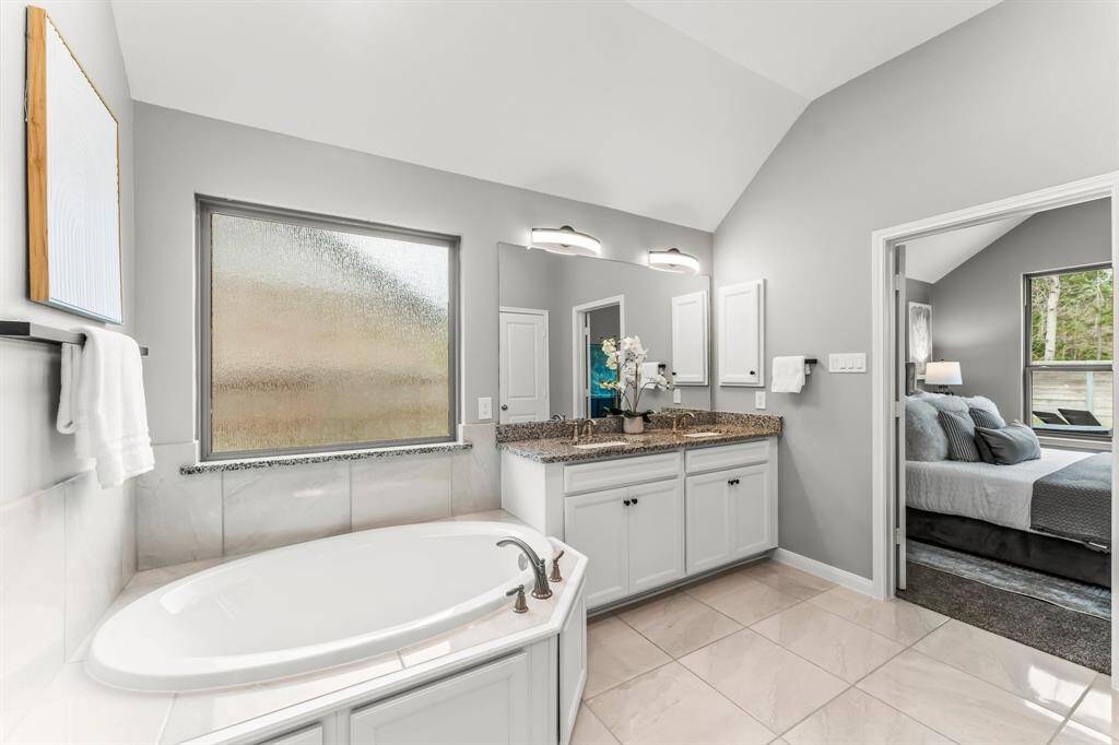 This photo shows a modern shower with elegant white tiles, a sleek rainfall showerhead, and a handheld sprayer. It features a granite bench and built-in shelving for convenience.