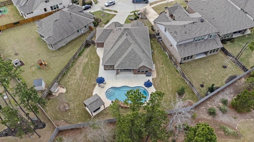 This aerial view showcases a spacious home with a large backyard featuring a beautifully designed pool and patio area. The property is situated in a cul-de-sac with well-maintained landscaping and ample driveway space.