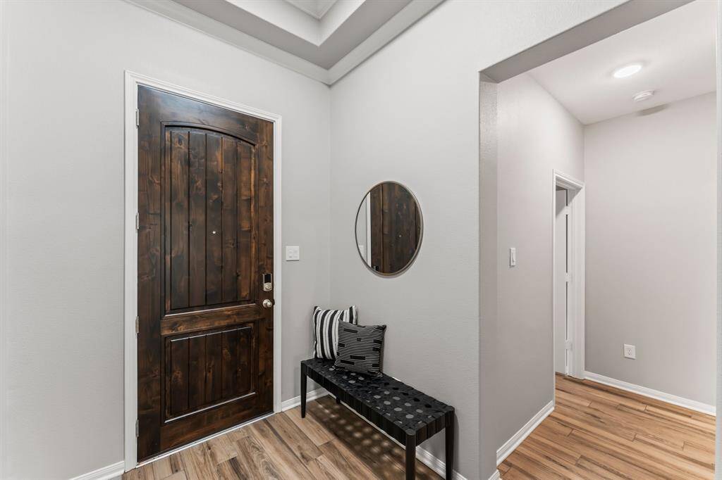Step into this classic entryway, where a wood-look tile floor and elegant tray ceiling set the tone. The hallway opens to a bright living area, framed by large windows that flood the space with natural light.