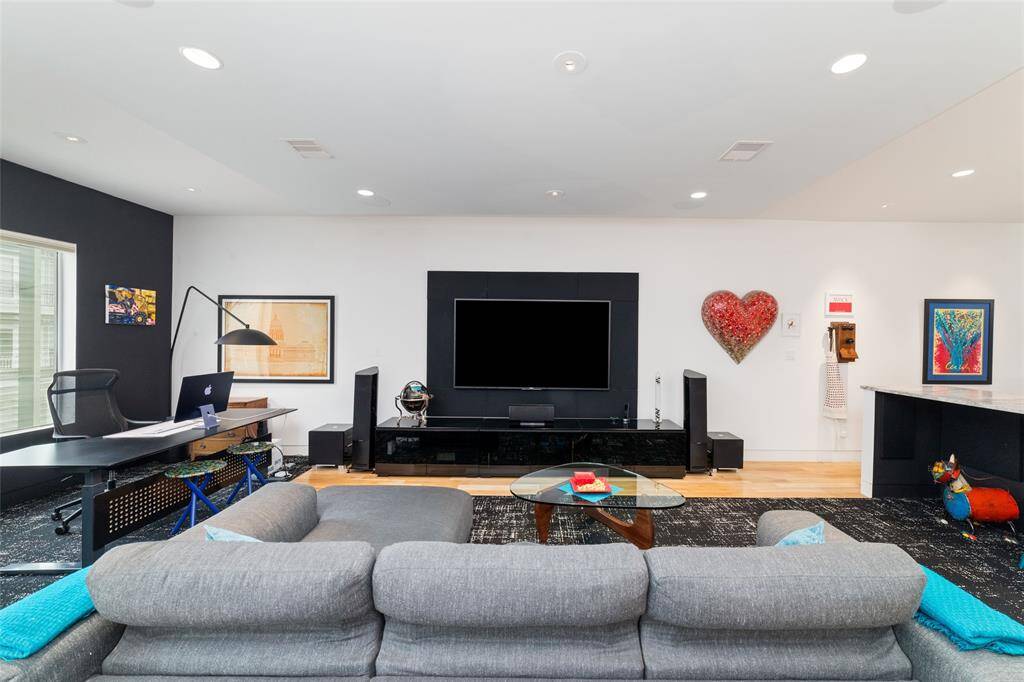 The large living room is designed for entertainment, with an 85" television framed by acoustic panels, ceiling speakers, and wiring for surround sound. The TV and acoustic wall panels will convey with the home.