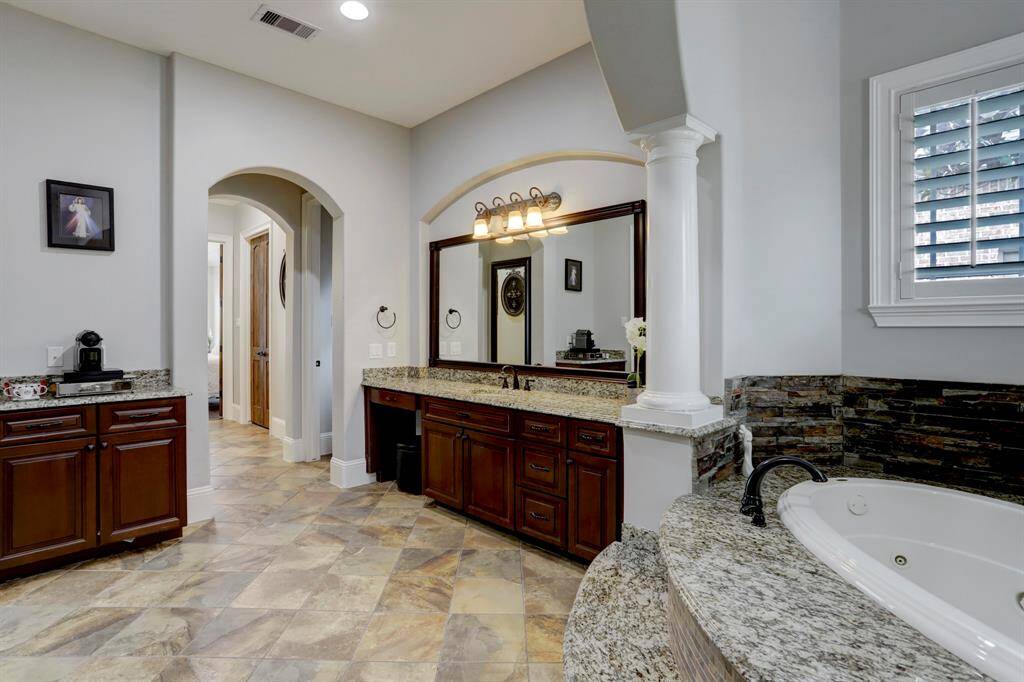 The arched doorway provides a smooth transition into the adjoining corridor, while the  column accentuates the partial-height soffit above the tub deck, creating an intimate alcove. The custom millwork of the dual-sink vanity integrates with granite countertops for durability, and the large framed mirror further enhances spatial depth. Arched portals, recessed lighting, and a neutral wall color complete the design, balancing classical influences with contemporary practicality.