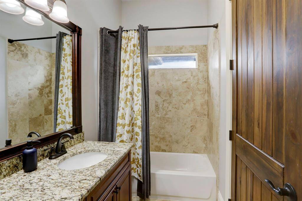 The tub-shower combo is clad in neutral tile that adds a subtle yet refined touch, while oil-rubbed bronze fixtures lend timeless appeal. A large framed mirror and stylish lighting maximize brightness and functionality, making this space both practical for everyday use and inviting for guests.