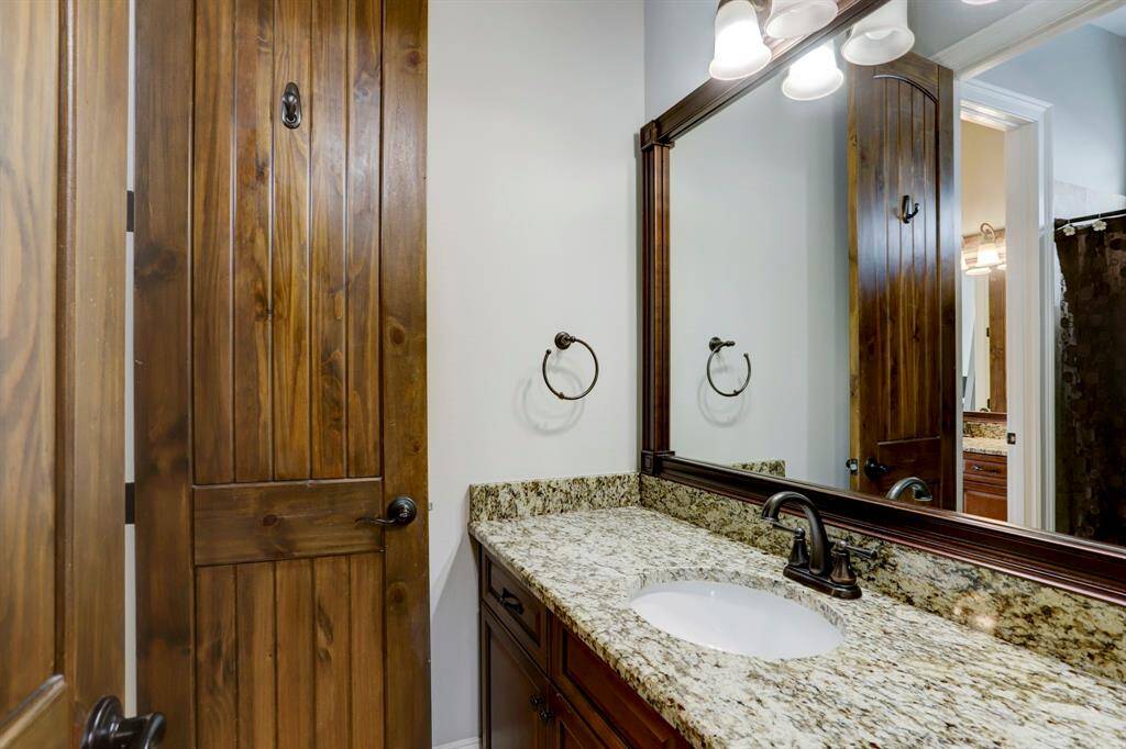 This secondary bathroom exudes warmth and elegance, featuring a rich wood door that adds natural character. The granite countertop and matching backsplash complement the wood cabinetry, creating a cohesive, upscale look. The oil-rubbed bronze fixtures and hardware tie the design elements together, giving the bathroom a timeless appeal.