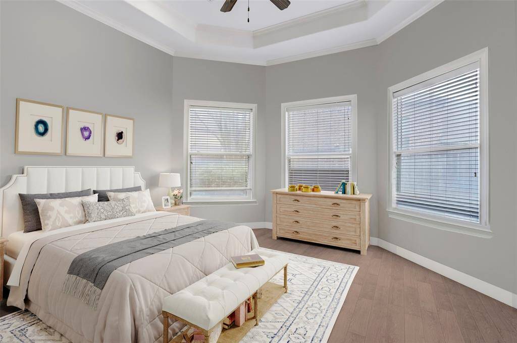 This bright and airy secondary bedroom features a beautiful tray ceiling that adds architectural interest, while the neutral gray walls and large windows create a welcoming, open feel. With abundant natural light and a soothing color palette, this room is a versatile retreat for family or guests. (Digitally Staged)