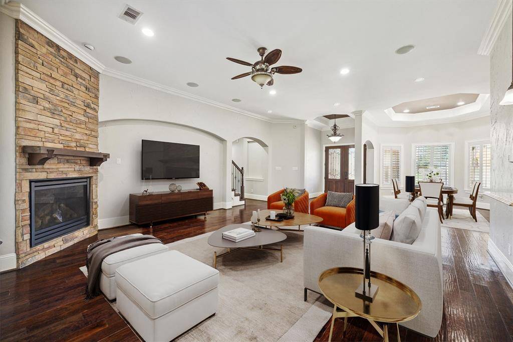 Step into the inviting living area, where elegant crown molding, rich wood flooring, and striking archways create a warm and sophisticated ambiance. A stylish ceiling fan enhances comfort, while the stunning stone-wall fireplace serves as a beautiful focal point. (Digitally Staged)