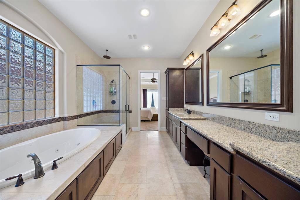 The spacious master bathroom features a large tub, a glass-enclosed shower, dual vanities with ample countertop space, and a frosted glass window providing natural light.