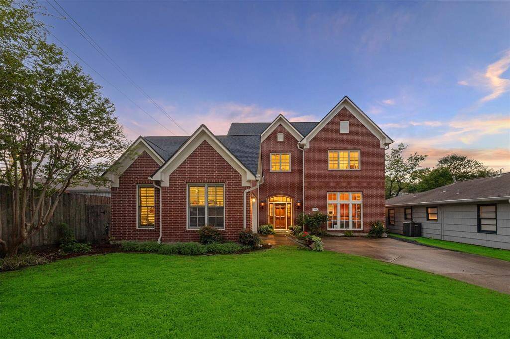 This is a two-story brick home featuring a prominent gable roof, large windows, and a welcoming front door with sidelights. The property includes a well-maintained lawn and is captured during dusk, highlighting its exterior lighting and peaceful neighborhood setting.