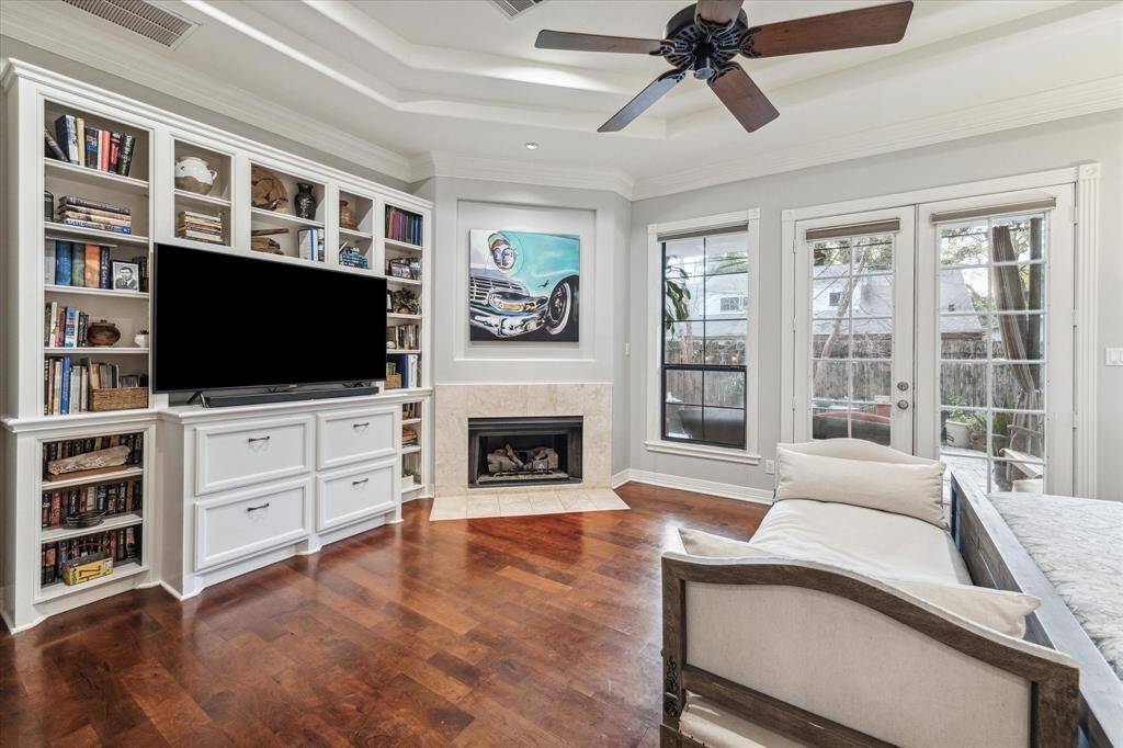 Enjoy a large, bright, tranquil primary bedroom with built-in bookshelves, a fireplace, hardwood floors, and French doors leading outside, complemented by a tray ceiling 11' at it's peak.