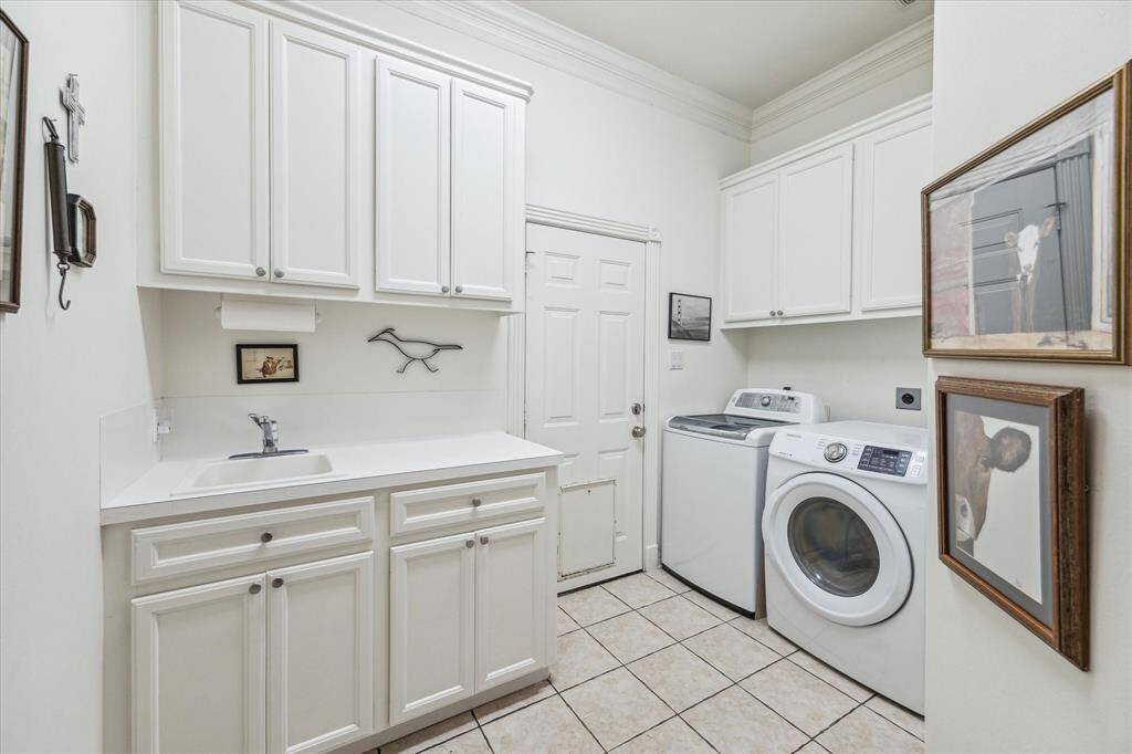 This is a functional laundry room features white cabinetry, a sink, and amble storage. The door leads to a long wide side yard which is currently used as a dog run.