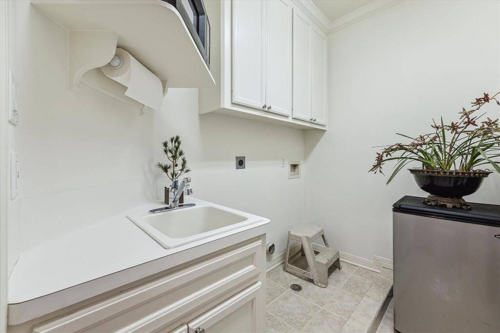 This is the second floor utility room.  It features a sink with storage below, white cabinetry.  There are washer/dryer hookups and it currently has a small refrigerator and microwave as it is just off the game room.