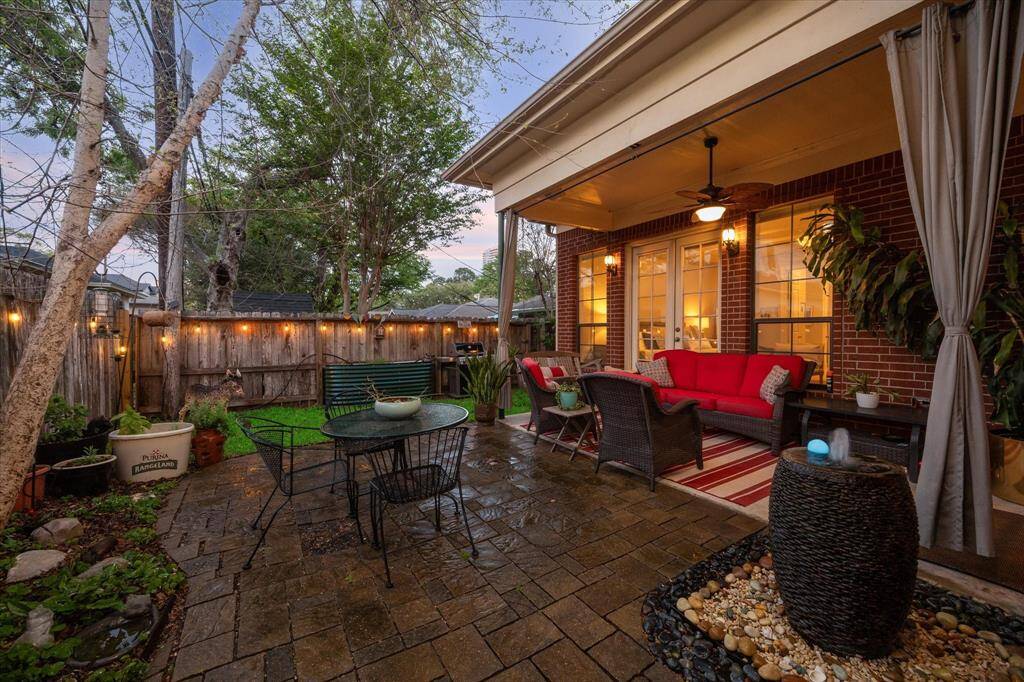 This is a cozy and inviting backyard patio with comfortable seating, ambient lighting, and lush greenery, offering a perfect outdoor space for relaxation and entertainment.