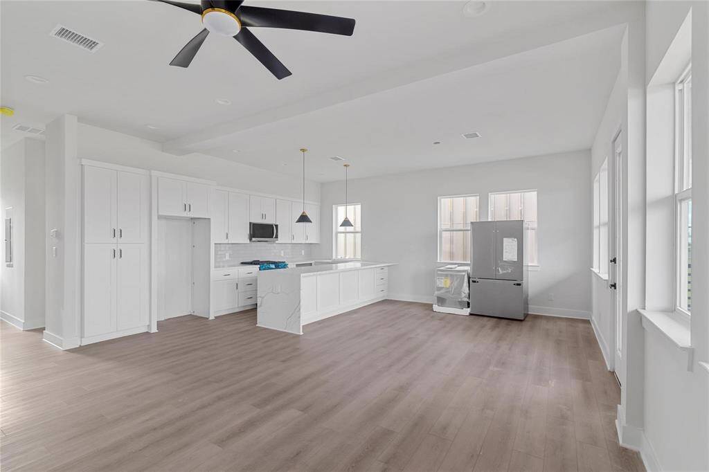 Lively common area features wood-look vinyl planks, a ceiling fan, and a neutral color palette, offering a canvas for personalization. (Refrigerator and dishwasher in image to be installed in appropriate slots in Kitchen)