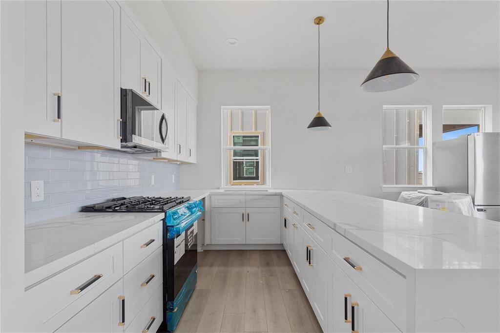 Cook up your meals in this bright kitchen featuring white shaker cabinets, waterfall quartz countertops, stainless steel appliances, a gas stove, and contemporary pendant lighting. (Representative phot from a more finished home)